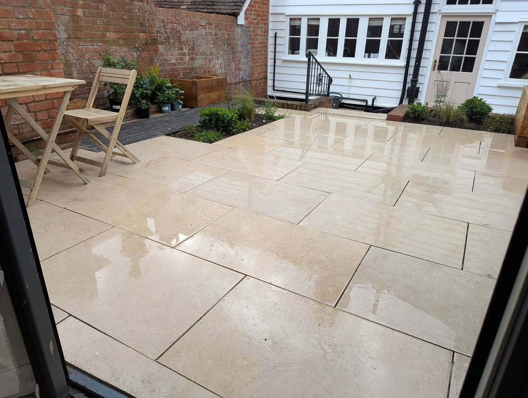 A new porcelain patio laid by Land & Mortar, wet after rain, garden furniture on it